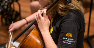 Op deze foto is een celliste van het NJO te zien met op de linkermouw van haar T-shirt het logo van Nationale Jeugdorkesten Nederland (NJON)